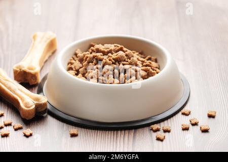 Un bol de nourriture pour chiens et de gâteries sous forme d'os sur un plancher en bois. Sécher les aliments en granulés. Banque D'Images