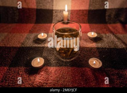 Panne. Crise énergétique. Destruction des infrastructures. Concept de coupure de courant. Une tasse transparente de tisane se tient dans un cercle de bougies allumées Banque D'Images