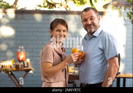 Couple heureux parlant et flirtant dans le jardin de la terrasse qui contient des cocktails. Les gens qui toaster le cocktail bellini et Aperol spritz ensemble à l'extérieur s Banque D'Images