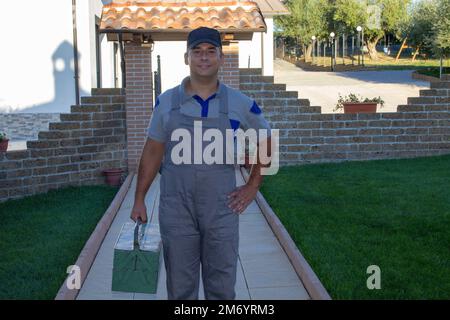 Image d'un homme à main dans des salopettes et une boîte à outils sur son chemin vers une maison pour des réparations. Banque D'Images