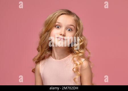 Une petite fille aux cheveux bouclés blonds, dans une robe rose pose pour l'appareil photo Banque D'Images