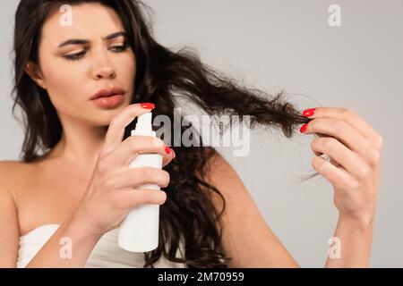 brunette femme pulvérisation produit de traitement sur cheveux endommagés isolé sur gris, image de stock Banque D'Images