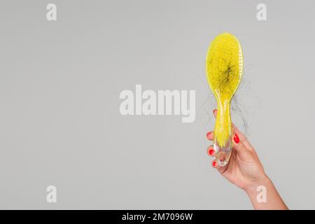 vue rognée de la femme avec manucure rouge tenant une brosse à cheveux jaune avec des cheveux perdus isolés sur gris, image de stock Banque D'Images