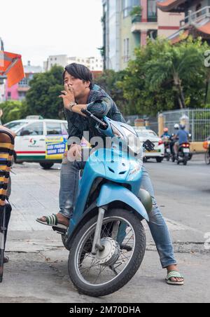 Ho Chi Minh ville, Vietnam - 2 octobre 2019 : le gars s'assoit sur une moto et fume une cigarette. Banque D'Images