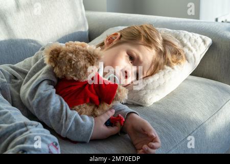 Portrait en gros plan de bébé garçon tenant et nourrissant le lait du biberon allongé sur le canapé. Un petit garçon mignon avec une bouteille de lait. Temps de sommeil. Banque D'Images