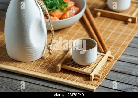 Saké japonais et saumon sashimi et algues wakame sur un tapis de bambou Banque D'Images