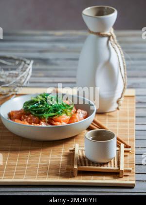 Saké japonais et saumon sashimi et algues wakame sur un tapis de bambou Banque D'Images