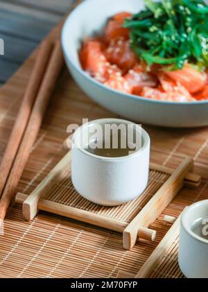 Saké japonais et saumon sashimi et algues wakame sur un tapis de bambou Banque D'Images