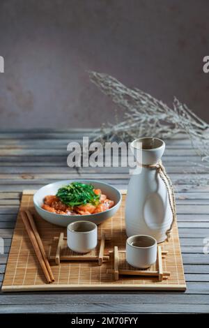 Saké japonais et saumon sashimi et algues wakame sur un tapis de bambou Banque D'Images