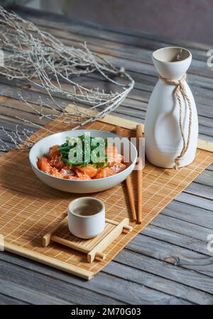 Saké japonais et saumon sashimi et algues wakame sur un tapis de bambou Banque D'Images