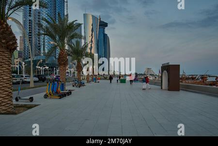 Photo de la corniche de Doha au coucher du soleil montrant les gratte-ciels de la baie ouest et la promenade avec les habitants et les visiteurs marchant Banque D'Images