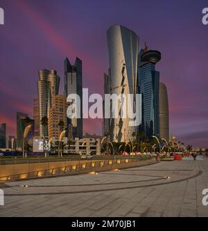 Photo de la corniche de Doha au coucher du soleil montrant les gratte-ciels de la baie ouest et la promenade avec les habitants et les visiteurs marchant Banque D'Images