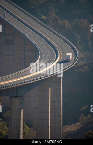 Viaduc énorme traversant un ravin avec un camion avec une semi-remorque réfrigérée roulant le long de la route. Banque D'Images