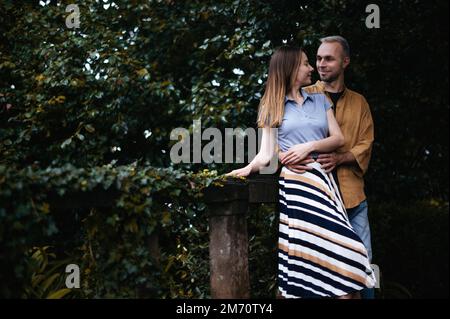 Une photo romantique d'un jeune couple debout dans un beau parc d'automne, embrassant et embrassant près d'un groupe de buissons Banque D'Images