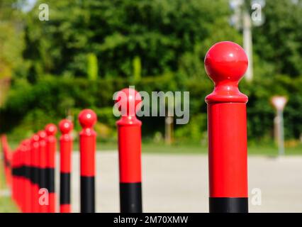 bornes ou bornes en acier rouge. vue de détail en gros plan. tête de tige en forme de sphère sur le dessus du tuyau en métal. fond vert luxuriant et doux. perspective décroissante Banque D'Images