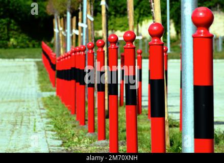 bornes ou bornes en acier rouge. vue de détail en gros plan. tête de tige en forme de sphère sur le dessus du tuyau en métal. fond vert luxuriant et doux. perspective décroissante Banque D'Images