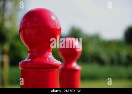 bornes ou bornes en acier rouge. vue de détail en gros plan. tête de tige en forme de sphère sur le dessus du tuyau en métal. fond vert luxuriant et doux. perspective décroissante Banque D'Images