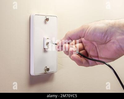 Un électricien mâle branche le cordon téléphonique de la ligne fixe dans la prise murale. Banque D'Images