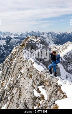 Alpiniste prenant des photos à la crête du sommet, randonnée à l'Ammergauer Hochplatte dans les Alpes d'Ammergau en hiver, montagnes enneigées, Bavière Banque D'Images
