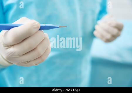 Gros plan du chirurgien tient un scalpel avec la poignée bleue dans sa main Banque D'Images