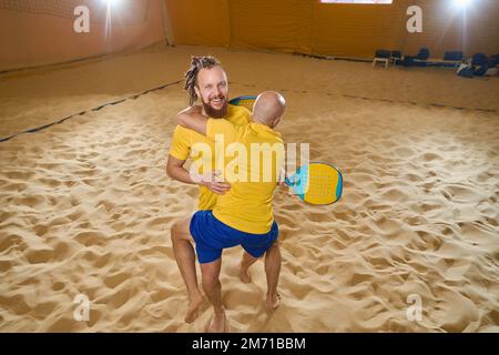 Les hommes sautent en couple tout en jouant au tennis de plage Banque D'Images