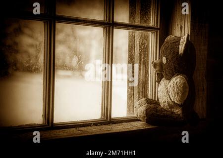 Une image de sépia-ton et de vignettage d'un ours en peluche fait main très vieux assis dans la fenêtre d'une cabine de pionnier historique abandonnée. Banque D'Images