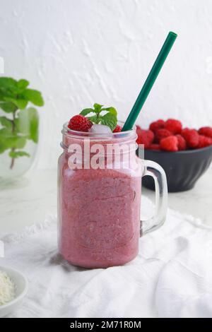 smoothie à la noix de coco et à la framboise avec glace dans un pot à la paille, fond blanc Banque D'Images