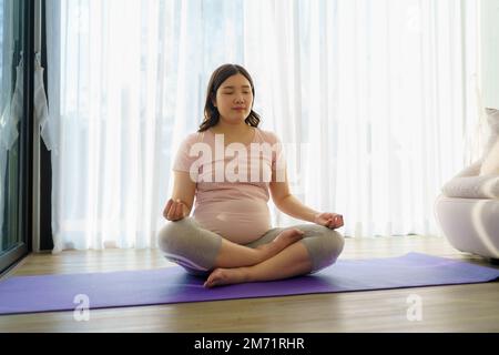 Portrait d'une femme enceinte asiatique pratiquant le yoga dans le salon à la maison. Banque D'Images