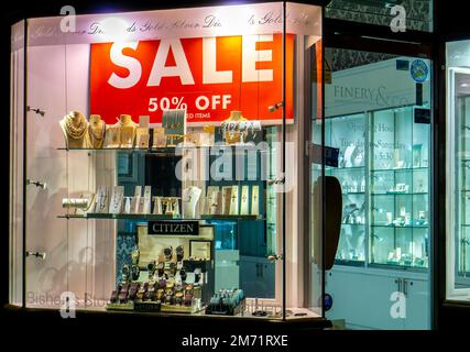 Grande affiche de vente dans une fenêtre de magasin de bijoux éclairée la nuit à Saffron Walden Banque D'Images