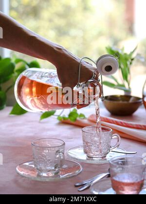 Verser le thé orange dans des tasses en verre sur fond rose Banque D'Images