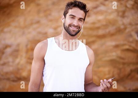 La musique me motive. un beau jeune homme debout à l'extérieur avec des écouteurs. Banque D'Images