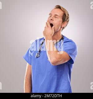 Sommeil après une longue chirurgie. Court studio photo d'un beau docteur bâillant. Banque D'Images