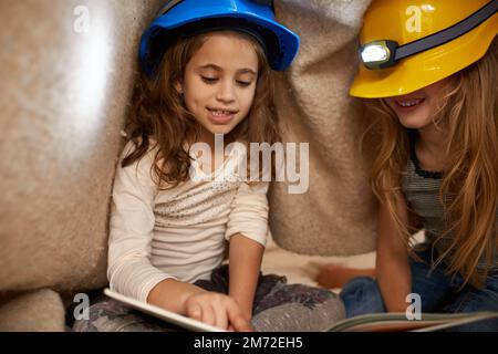 Lire leurs histoires préférées. deux petites filles lisant sous une couverture à l'aide de phares. Banque D'Images