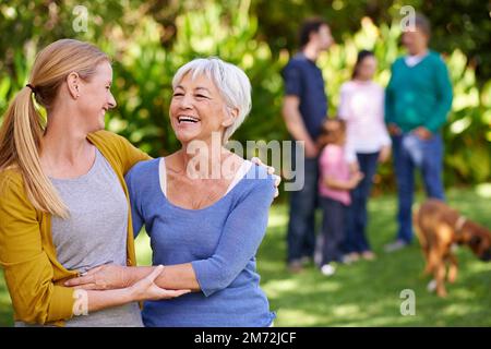 La famille passe avant tout. Portrait d'une jeune femme embrassant sa mère avec le reste de la famille en arrière-plan. Banque D'Images