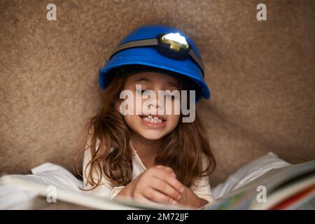 Se perdre dans l'histoire. une petite fille mignonne lisant sous une couverture à l'aide d'un phare. Banque D'Images