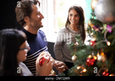 Qu'est-ce que vous pensez papa. une famille plaçant des ornements sur l'arbre de noël. Banque D'Images