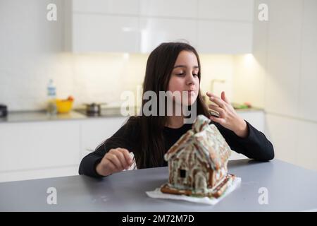 Enfants avec maison de pain d'épice, Une fille adolescente est en train de manger une maison de pain d'épice Banque D'Images