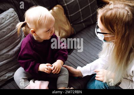 Vue de dessus de la magnifique petite fille blonde enfant assis sur un canapé, regardant les enfants médecin examinant le patient à la maison. Banque D'Images