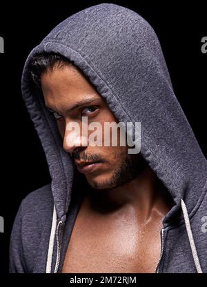 Il a son œil sur vous. Court studio photo d'un jeune homme concentré portant un sweat à capuche isolé sur le noir. Banque D'Images