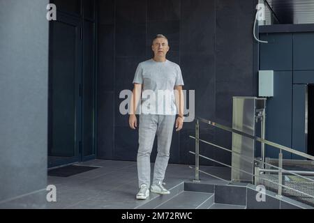 Prise de vue en longueur d'un homme aux cheveux gris confiant qui marche près des marches d'entrée du bâtiment. Gestion de la profession pour les aînés Banque D'Images