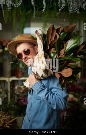 Concept de la Saint-Valentin ou de la Journée internationale de la femme. Race de race blanche dans des lunettes de soleil et chapeau tenant grand bouquet de fleurs de printemps frais dans magasin de fleurs. Image verticale de haute qualité Banque D'Images