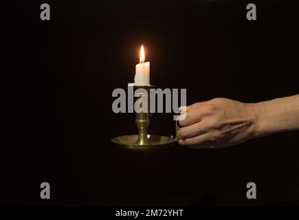 Chandelier décoratif en cuivre avec bougies allumées dans une main femelle sur fond noir Banque D'Images