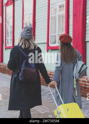 Vue arrière deux joyeuses touristes souriant et marchant avec des valises dans la rue de la ville en automne ou au printemps - Voyage et concept de vacances Banque D'Images