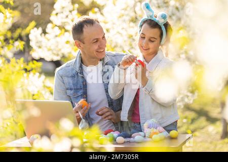 père et fille colorant des œufs de pâques avec un ordinateur portable dans le jardin Banque D'Images