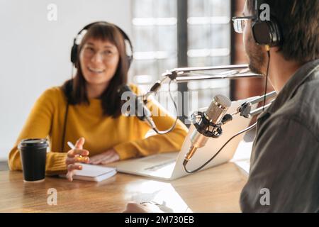Deux jeunes baladodiffusion dans des écouteurs pour l'enregistrement et la diffusion de podcasts en studio. Femme et homme faisant un podcast audio en direct, exécutant leur émission radio à l'aide de microphones. Mise au point sélective sur le microphone Banque D'Images