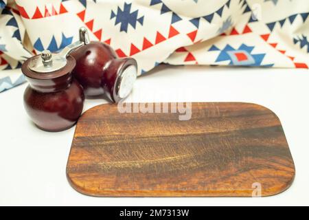 Planche à découper en bois avec moulin à sel et poivre à côté d'une serviette en tissu, mise au point douce gros plan Banque D'Images