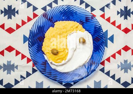 polenta ou mamamaliga avec fromage cottage sur une assiette de verre bleu, placage du symbole yin et yang, vue du dessus Banque D'Images