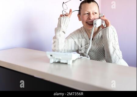 Une femme d'âge moyen souriante parle au téléphone sur son lieu de travail Banque D'Images