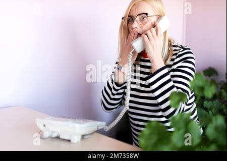 choqué femme d'âge moyen parlant sur un téléphone fixe à son lieu de travail Banque D'Images