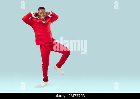 Joyeux homme afro-américain excité en costume rouge dansant sur fond bleu clair de l'espace de copie Banque D'Images